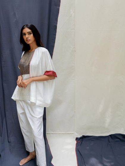 A white peplum-style top with voluminous sleeves and a textured grey panel, paired with slim white trousers.