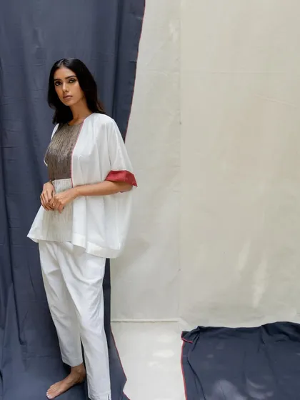 A white peplum-style top with voluminous sleeves and a textured grey panel, paired with slim white trousers.