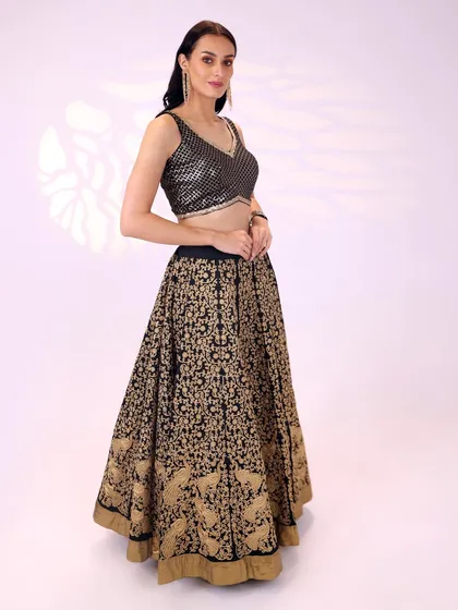 A side profile of the black and gold lehenga, highlighting the A-line silhouette of the skirt and the intricate pattern work that covers it.