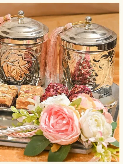 Every detail speaks the language of love. This hamper from my wedding edit features rose petal ladoos, nut brittles, and embossed silver jars, all beautifully arranged with silk flowers.