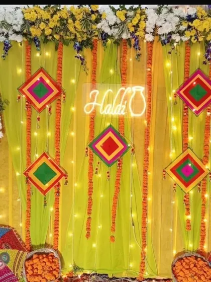 A festive Haldi backdrop with a neon sign and colorful hangings. The design uses bright yellow drapes, marigold garlands, and Rajasthani umbrellas for a vibrant and celebratory look.