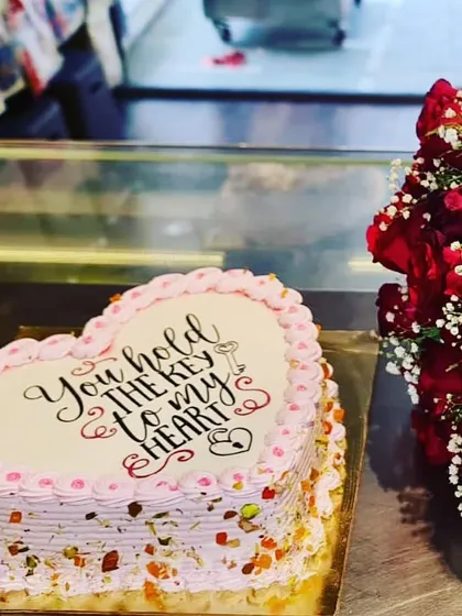 A beautiful heart-shaped cake paired with a bouquet of red roses. The cake, which says "You hold the key to my heart," is elegantly decorated with chopped nuts and pink piping, making it a complete romantic gift.