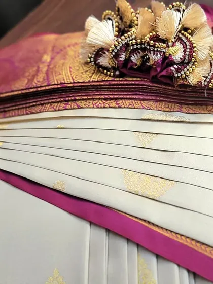 A close-up of a pre-pleated bridal saree, ready to be packed. The pleats are perfectly aligned and secured, and the pallu is adorned with a beautiful tassel.