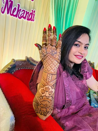 A happy client proudly showing off her full-arm mehndi. The design is a classic Rajasthani style with heavy jaal work and floral patterns, perfect for a wedding celebration.