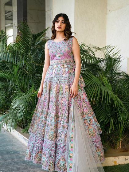 An ivory peplum achkan lehenga with intricate, multi-colored cut work and hand embroidery. This unique silhouette is a modern take on traditional wear, perfect for a fashion-forward wedding guest.