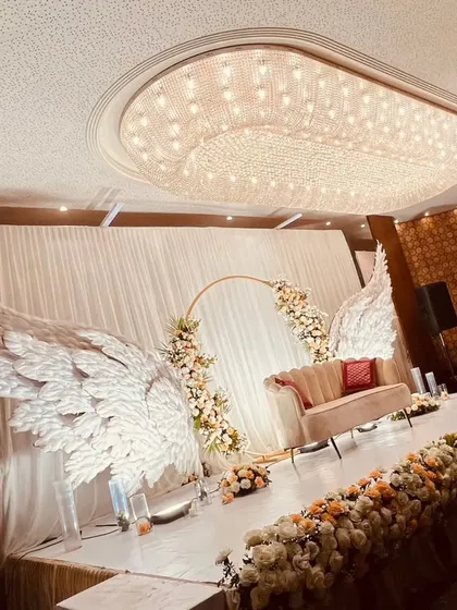 A truly angelic stage design featuring magnificent white wings flanking a central floral ring. This unique and ethereal concept creates a heavenly photo opportunity and a memorable focal point for the event.