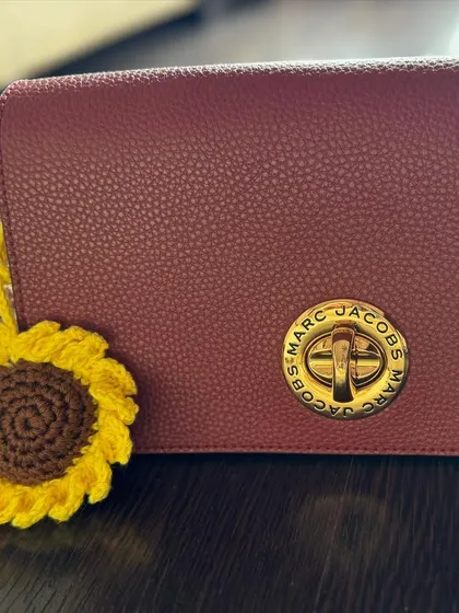 This vibrant crochet sunflower charm adds a bright, cheerful touch to a deep red handbag. It's a perfect accessory to brighten your day.