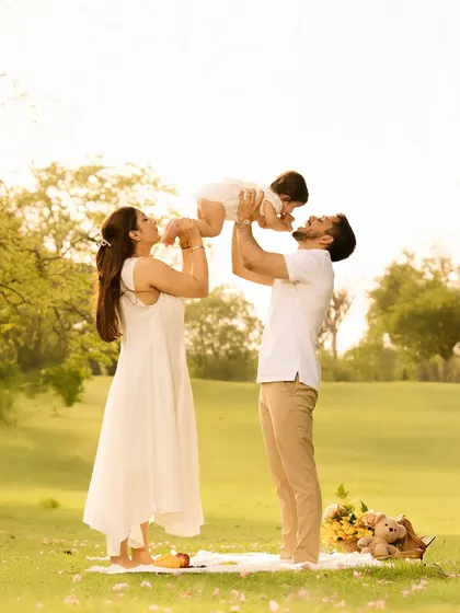 A father lifts his child towards the sun in a beautiful park, creating a classic, joyful pose that symbolizes love and aspiration. The warm, natural light enhances the emotional feel of the photo.