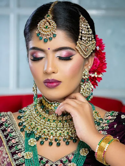 This bridal portrait highlights the beauty of contrast, pairing a deep velvet lehenga with striking emerald green jewelry. The makeup features a sharp wing and a bold lip to complete the powerful look.
