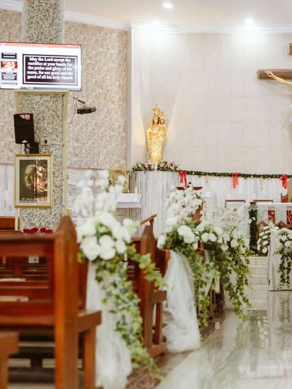 The aisle of the church, lined with beautiful arrangements of white flowers and greenery tied to the pews with sheer fabric. This creates a clean, elegant, and reverent path for the bridal procession.