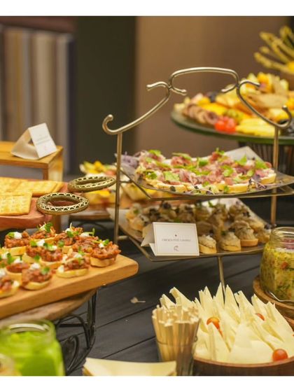A well composed shot of a tiered grazing display, showcasing different types of bruschetta, cheese sticks, and dips. The elegant metal stands add height and sophistication to the buffet layout.