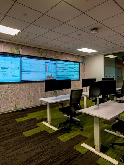 A small Network Operations Center (NOC) room with a large video wall for data monitoring. The design provides a focused, distraction-free environment for critical tasks.