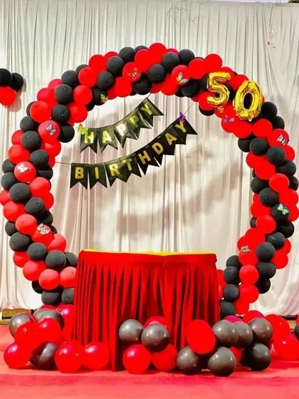 A bold red and black theme for a 50th birthday. This circular balloon arch frames a cake table, with a 'Happy Birthday' banner and a foil number '50' marking the milestone.