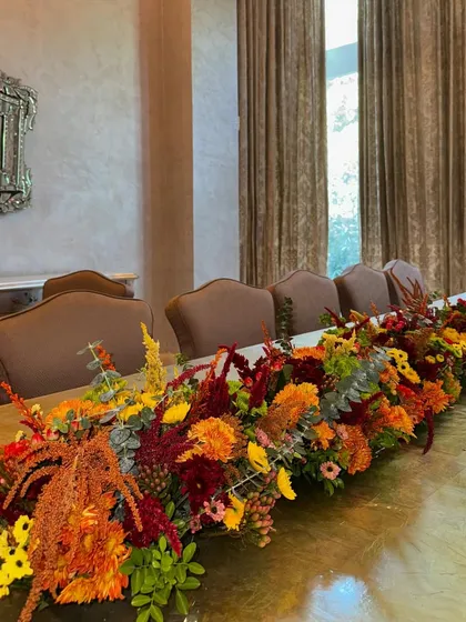 A long, autumnal flower runner designed to dress a dining table for the festive season. The warm tones of orange, red, and yellow create a cozy and inviting atmosphere as the days get shorter and the lights start to twinkle.