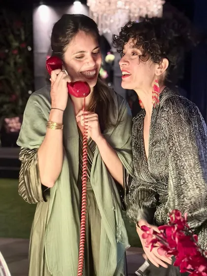 Capturing candid moments of connection and fun. Two guests share a laugh while leaving a joint message, showcasing the interactive and social nature of the audio guestbook experience at an evening sangeet or reception.