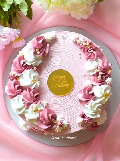 A top-down view of a floral cake with pink and white buttercream rosettes. This vanilla cake has a lovely textured finish and is dotted with small edible pearls.