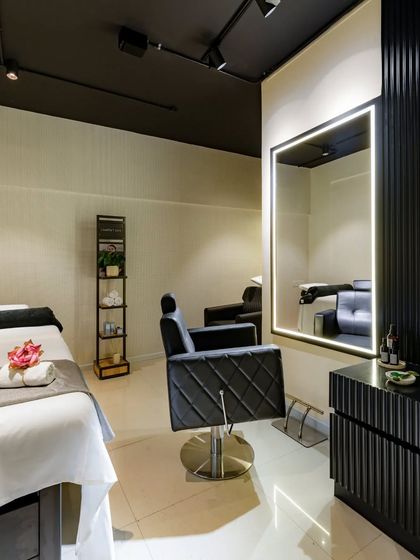 The hair-cutting station is designed for style and comfort. It features a luxurious tufted leather chair and a large, brightly lit mirror, set against a backdrop of black fluted panels and a dark ceiling for a dramatic, high-end look.