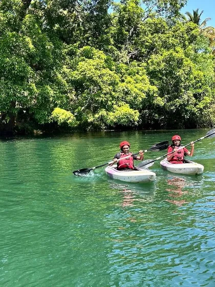 Two kayakers paddle in sync, exploring the lush riverbanks of Dandeli during a summer camp session.