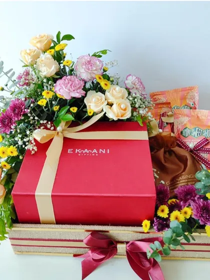 A custom wedding hamper designed with grandeur and grace. This gift features a large red box from Ekani, surrounded by a vibrant mix of roses, carnations, and other seasonal flowers.