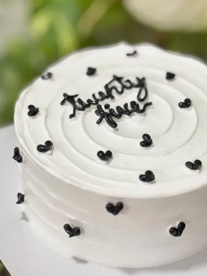 A close-up of the "twenty five" monochrome cake, highlighting the clean script and the simple, elegant black heart details.