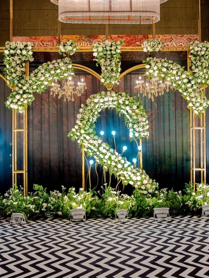 This stage features a striking black-and-white chevron floor leading to a backdrop of golden arches, white floral arrangements, and elegant chandeliers. It’s a bold, modern design suitable for a high-energy awards night or company celebration.