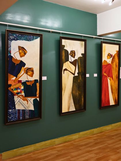 A view of our gallery with three figurative paintings by Bharti Prajapati against a dark green wall. The space is a conversation waiting to begin.