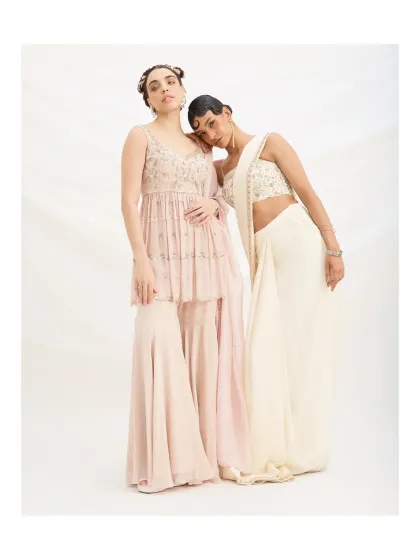 This image captures the soft elegance of the pastel sharara and a pre-draped ivory saree. Both outfits are designed for women who appreciate understated style and effortless movement.