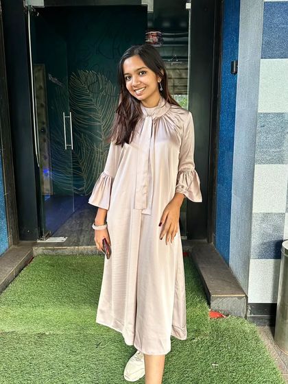 A full-length view of the custom satin formal dress. The simple, flowing silhouette combined with the chic tie-neck and bell sleeves makes for an effortlessly elegant outfit.