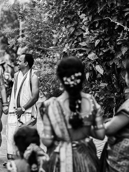 A black and white candid shot of the bride and groom walking with their family, capturing a natural, unposed moment.
