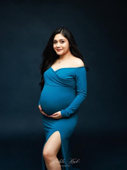 A beautiful portrait showcasing the vibrant teal gown against a deep blue background, highlighting the mother's serene glow.