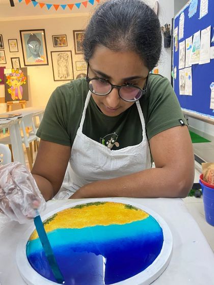 A participant carefully works on her resin beach art, adding details to the waves.