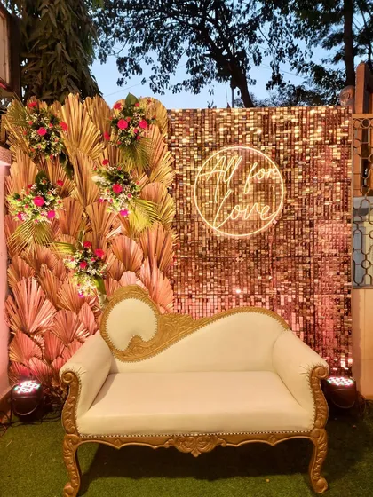 A glamorous photo booth for a Bollywood-themed night. The setup includes a gold sequin wall, a classic diwan, and a neon "All for Love" sign, perfect for capturing star-studded pictures.