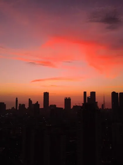 The Mumbai skyline is silhouetted against a deep purple sky with a large, soft red cloud formation.