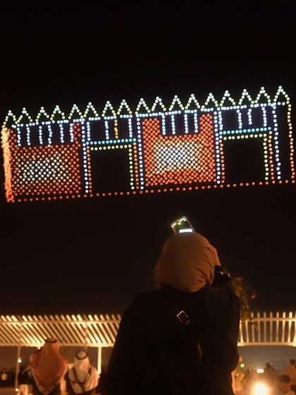 An audience watches our drone formation of a traditional Kuwaiti building. We specialize in creating detailed architectural renderings that celebrate local heritage during our international shows.