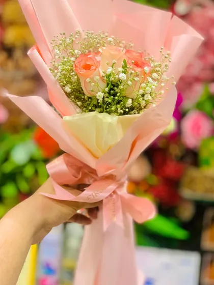 A delicate bouquet of peach-colored roses surrounded by baby's breath. The soft pastel tones and pink Korean-style wrapping create a gentle and charming floral gift.