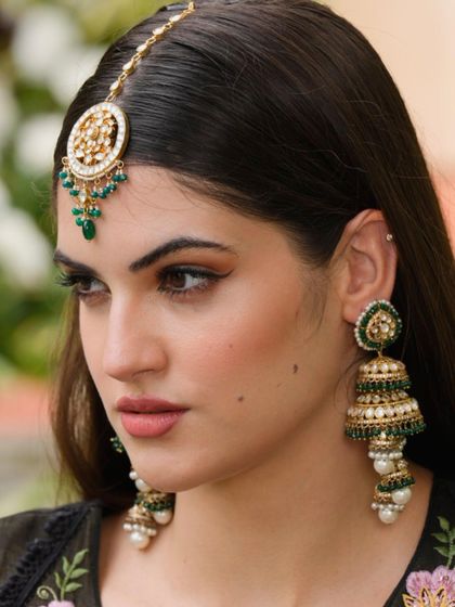 Slay every wedding event with rental jewels that make you glow. This model showcases a beautiful green and gold jhumka and maang tikka set.