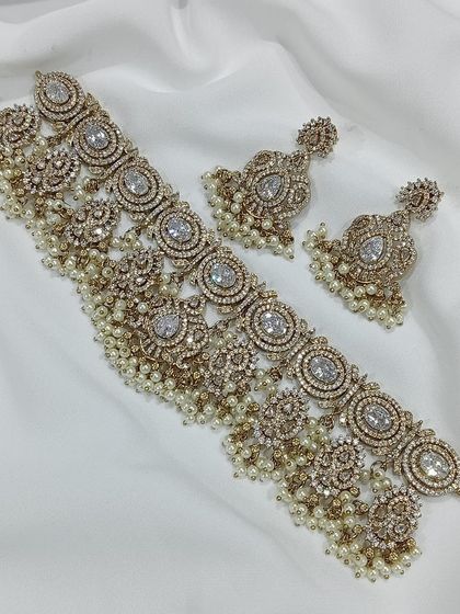 This choker set is available in multiple colors including ruby, emerald, and grey. The intricate metalwork combined with colored stones and pearl or bead droppings offers a sophisticated and royal look.