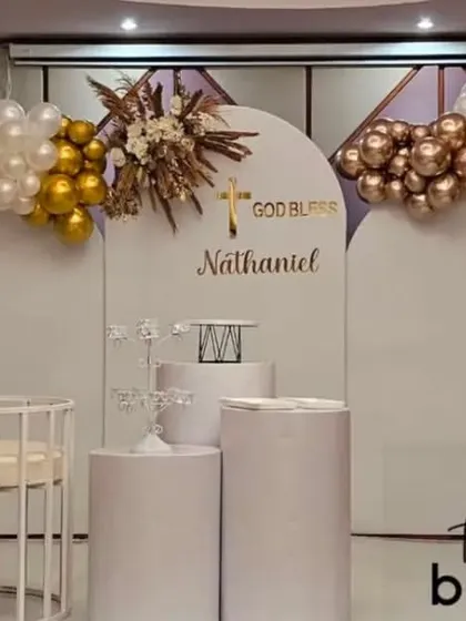 A beautiful 'God Bless Nathaniel' baptism party decoration. This clean and modern setup uses white backdrops with balloon arrangements in white, gold, and rose gold.