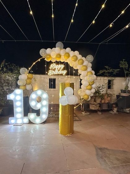 A beautiful rooftop setup for a 19th birthday. The gold and white balloon arch, fairy lights, and light-up numbers create a magical ambiance against the night sky.