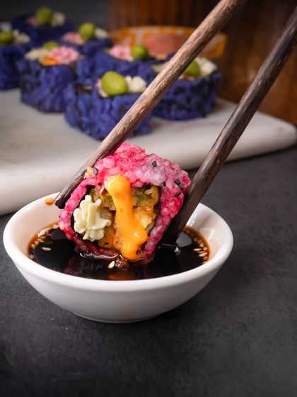 A perfect bite of the Pink Rice Assorted Tempura roll being dipped into soy sauce.
