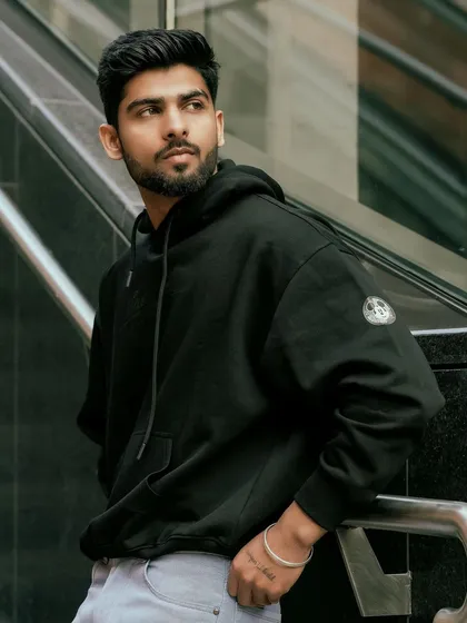A male model in a black hoodie, leaning against a railing in an urban setting. This showcases a modern, streetwear look that is popular for many brand campaigns.