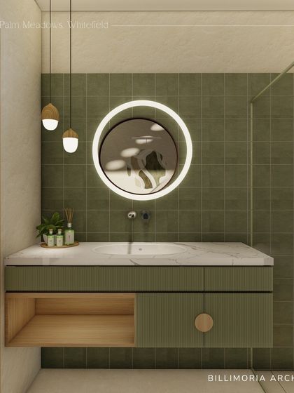 We used olive green square tiles to create a feature wall in this bathroom. The floating vanity combines a marble top with a wooden drawer, and the round backlit mirror and pendant lights complete the modern, earthy look.