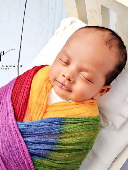 A baby boy sleeping in a miniature bed, wrapped in a vibrant rainbow swaddle.