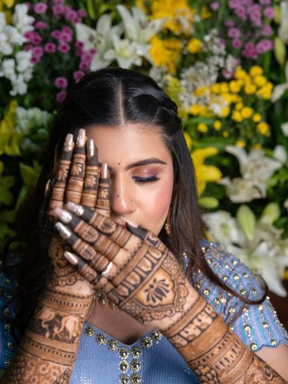 A creative pose highlighting the detailed henna work on the bride's hands. The floral background adds a touch of romance to the shot.