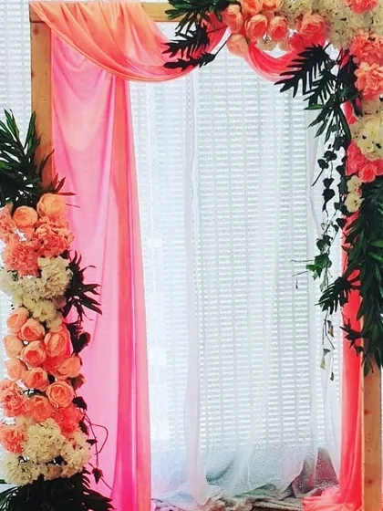 A simple wooden arch with peach fabric and floral arrangements, suitable for a photo booth or entrance.