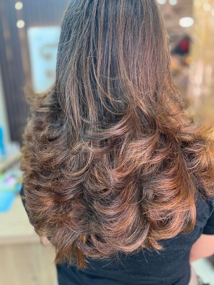 A beautiful example of a layered cut with a mix of caramel and honey-toned highlights, styled into soft, bouncy curls.