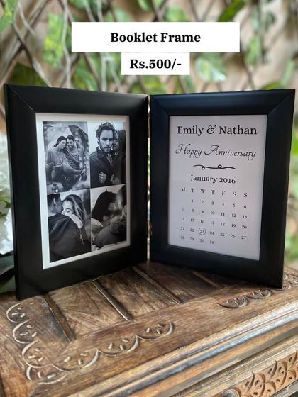 A closer look at the anniversary booklet frame. One side features a collage of four photos, while the other has a calendar marking the special day, all in a sleek black folding frame.