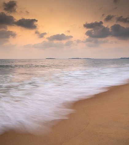 The waves on a sandy beach are blurred into a soft mist by a slow shutter speed, creating a minimalist and serene composition.