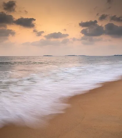 The waves on a sandy beach are blurred into a soft mist by a slow shutter speed, creating a minimalist and serene composition.