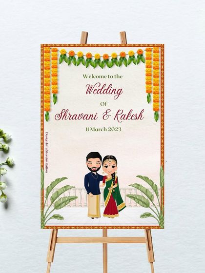 A traditional and charming welcome sign for Shravani and Rakesh's wedding. The design features a marigold toran, banana leaf illustrations, and a cute couple caricature dressed in South Indian wedding attire.